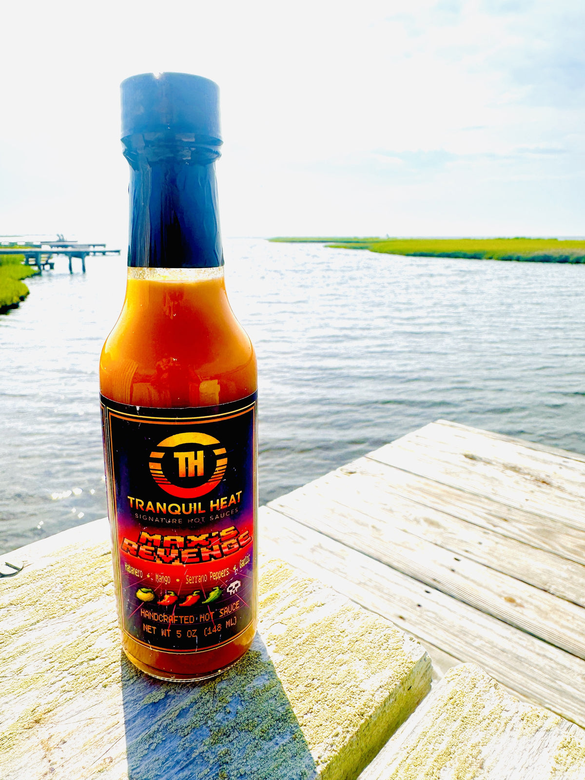 Bottle of Tranquil Heat Max's Revenge hot sauce on a dock overlooking a marsh