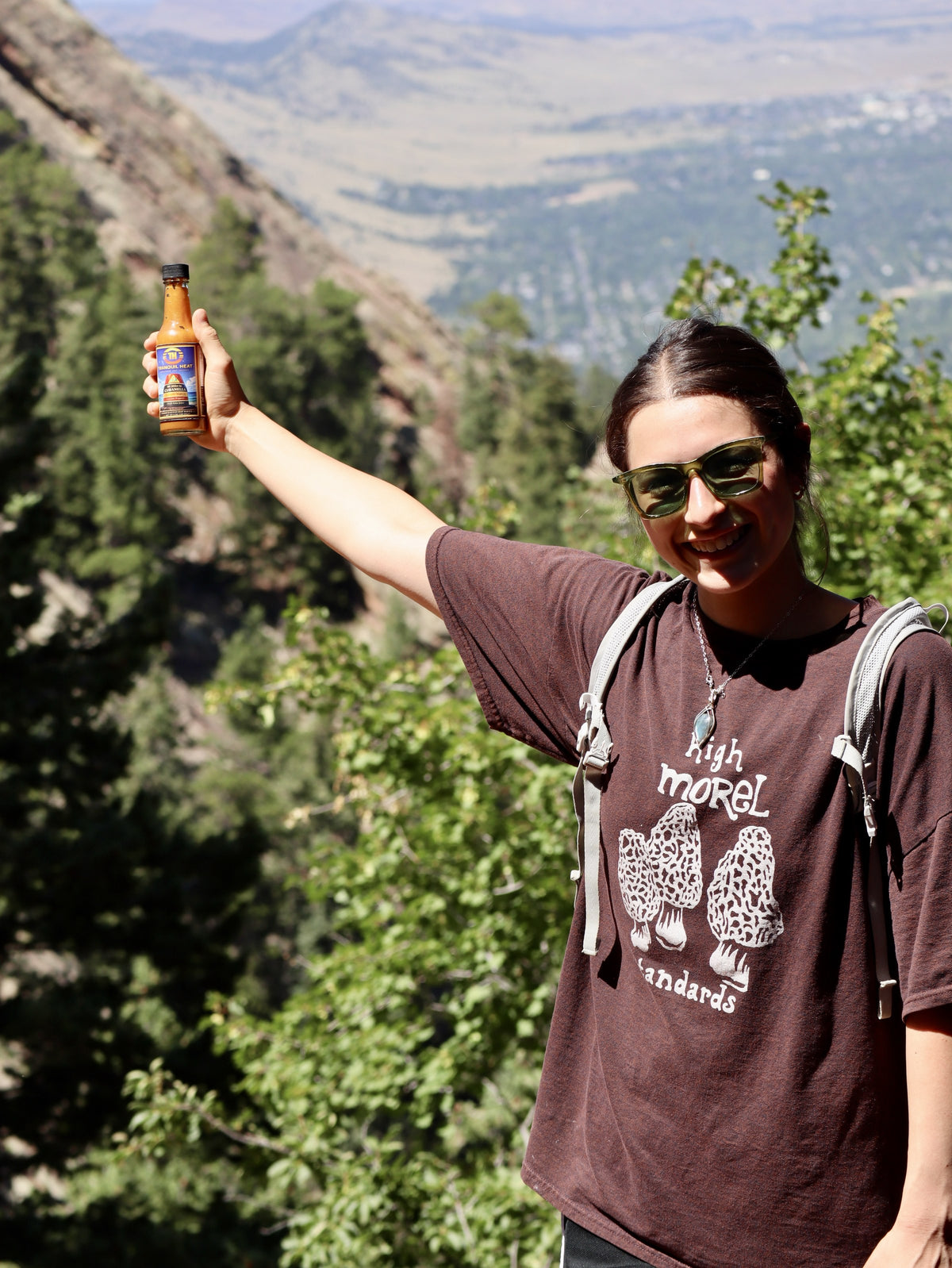 Hiker holding a bottle of Tranquil Heat hot sauce overlooking a mountain valley