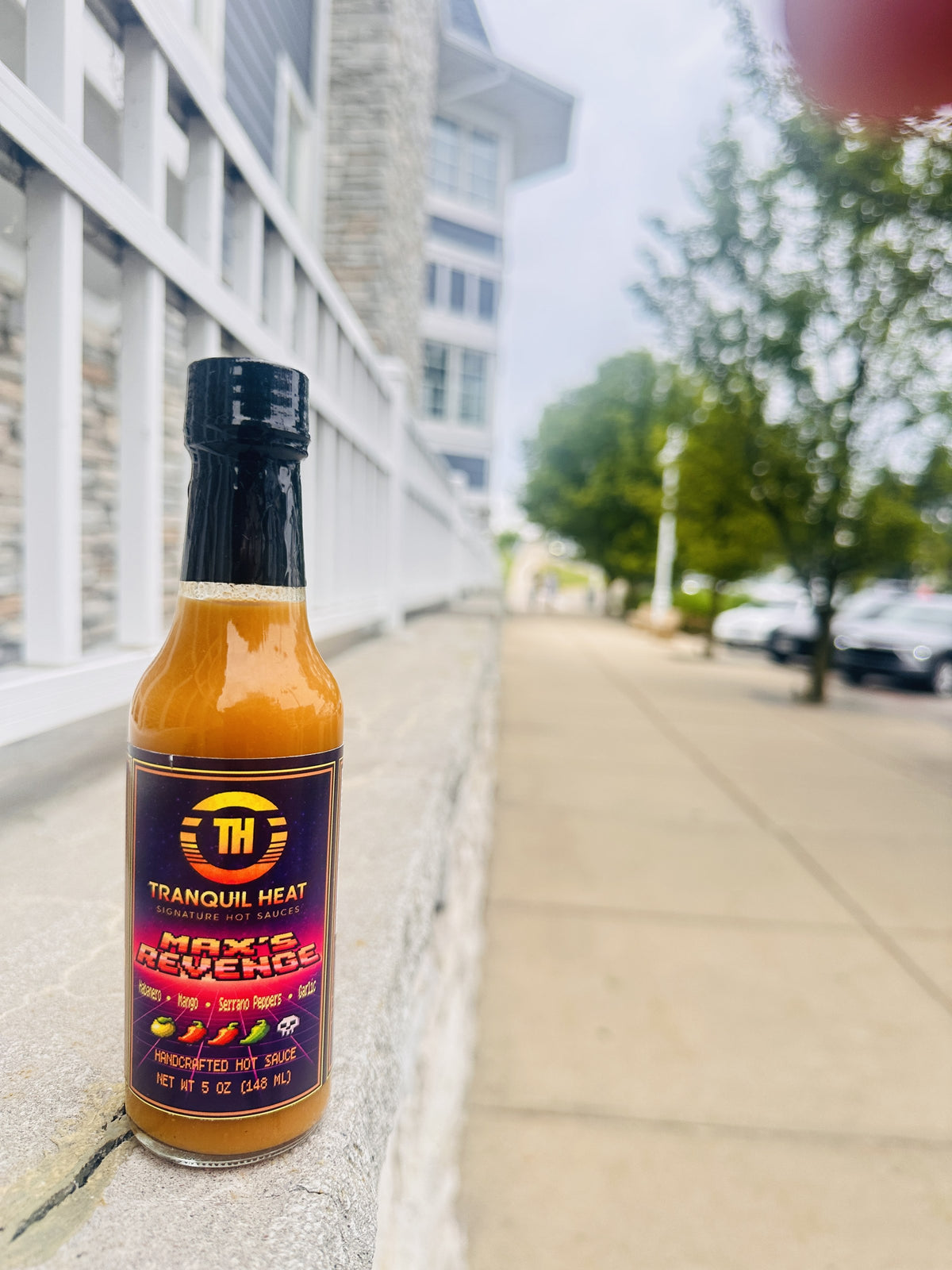 Bottle of Tranquil Heat Max's Revenge hot sauce on a sidewalk railing on Mackinac Island