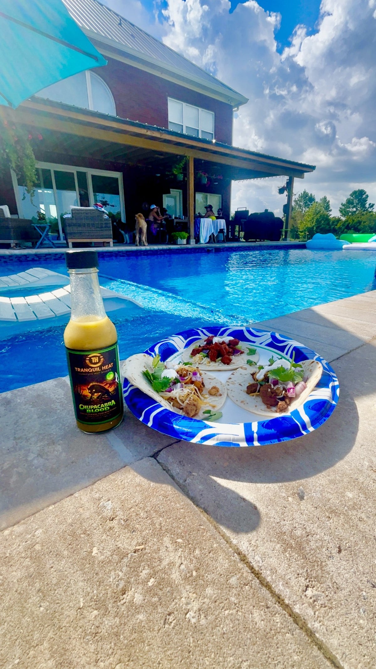 Bottle of Tranquil Heat Chupacabra Blood hot sauce next to a plate of tacos by a backyard pool