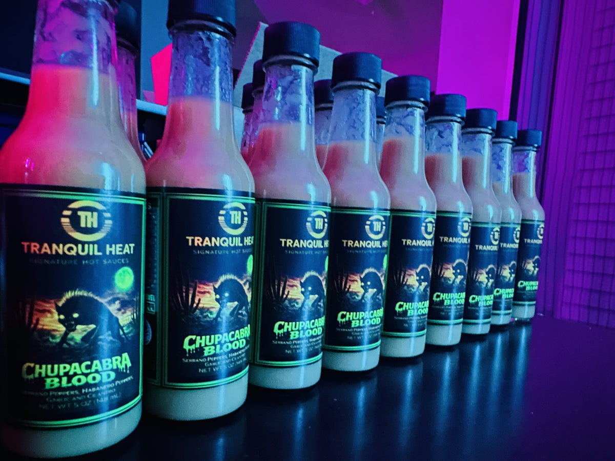 Row of Tranquil Heat Chupacabra Blood hot sauce bottles glowing under purple UV blacklight